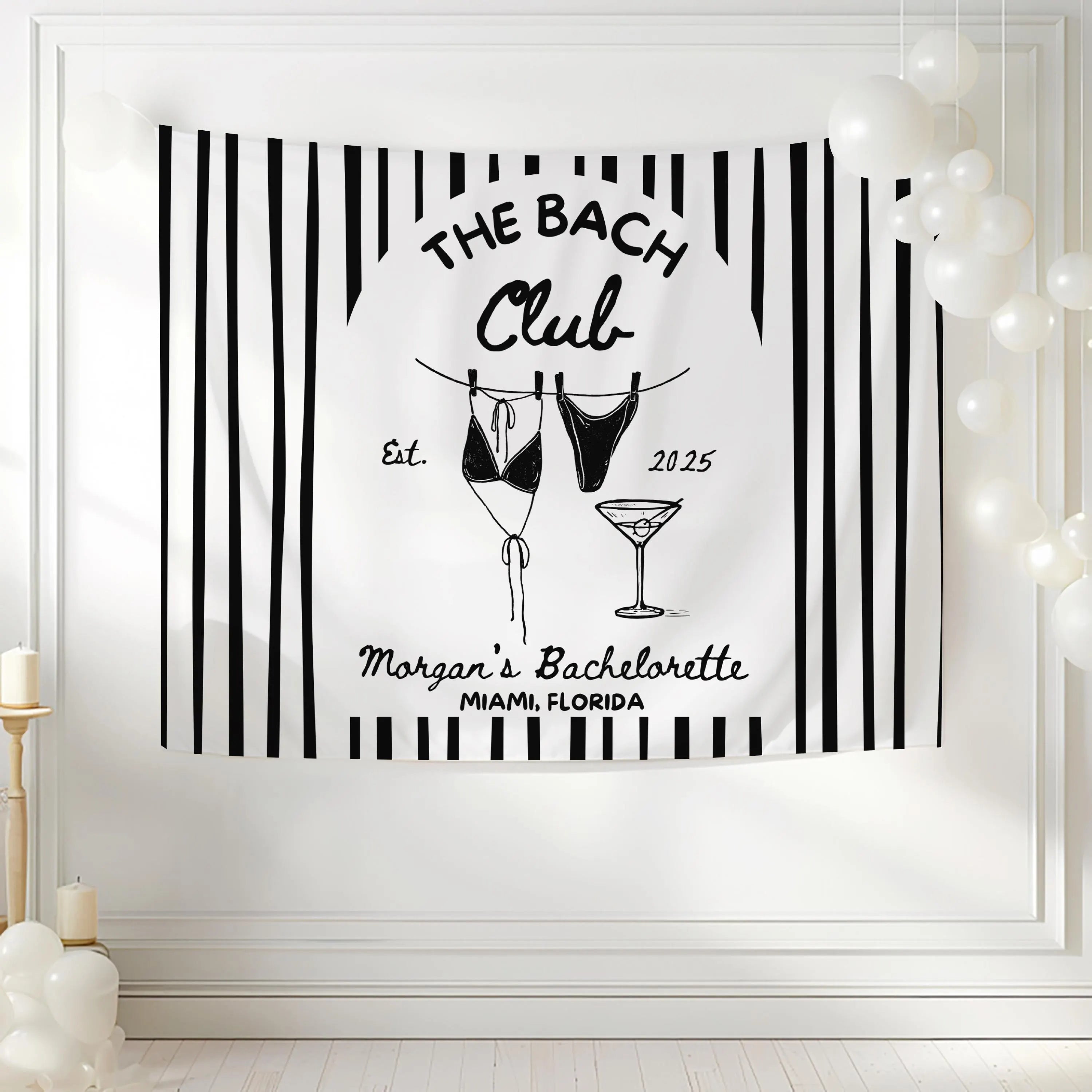 Coastal bachelorette backdrop with striped design, swimsuit clothesline artwork and personalized bride weekend decorations.